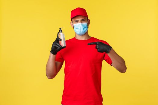 Covid-19, delivery orders, shopping, contactless handling and social distancing concept. Courier, takeaway employee in red uniform and medical mask, pointing at hand sanitizer.