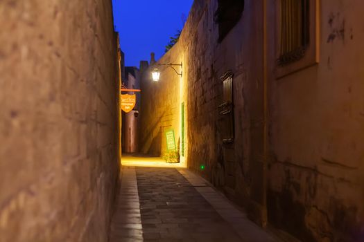 MDINA, MALTA - February 19, 2010. Illuminated narrow streets with cafes and restaurants. Night view on buildings and wall decorations of ancient town.