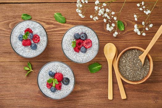 Chia pudding with fresh berries raspberries, blueberries. Top view, three glass on brown wooden background.