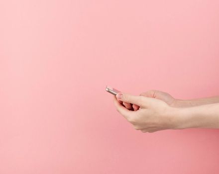 woman hand without manicure hold phone on pastel pink background with copy space