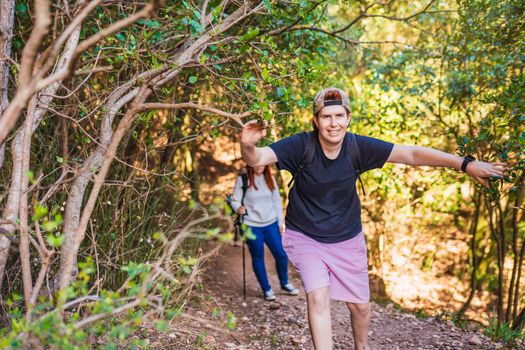 two young women friends hiking amateur, en route on a forest trail. hikers reaching the top. people on a trip. woman walking in nature. background of a lush forest, with green plants illuminated by sun rays.