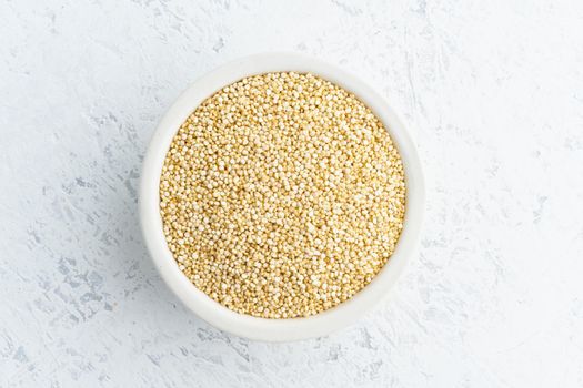 Quinoa seed in a white bowl on white background. Dried cereals in cup, vegan food, fodmap diet. Top view, close up.