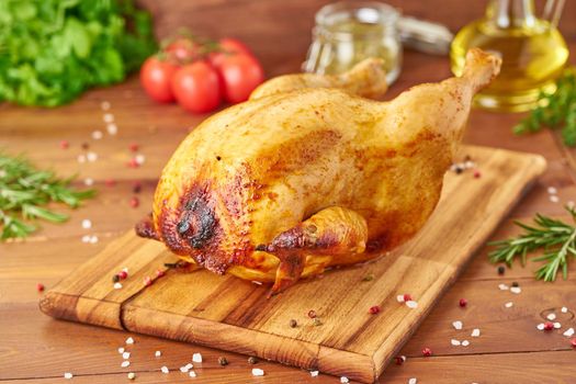 Whole roasted chicken on wooden cutting board on dark brown wooden table, side view