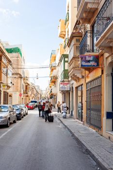 SLIEMA, MALTA - February 12, 2010. Tourists with suitcases are walking up the street.