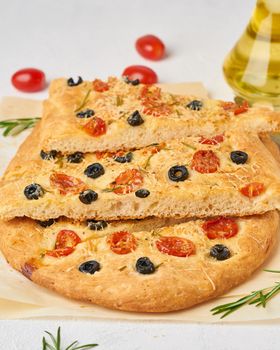 Focaccia, pizza, chopped italian flat bread with tomatoes, olives and a rosemary. Vertical, side view.