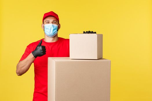 Express delivery during pandemic, covid-19, safe shipping, online shopping concept. Proud and confident courier assure packages are safe, thumb-up as stand near boxes with parcels.