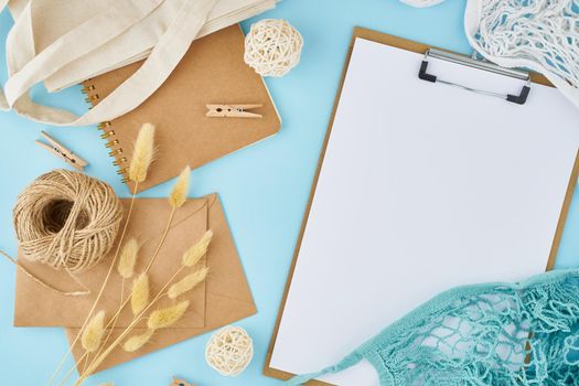 Zero waste concept. White sheet on clipboard, craft envelopes, bag, string bag, on a bright blue office modern desktop. Environmentally friendly and natural mock up