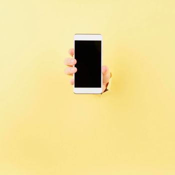 unrecognizable person showing smartphone in bursted hole in pink cardboard, copy space