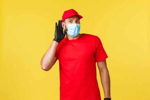 Express delivery during pandemic, covid-19, safe shipping, online shopping concept. Intrigued courier overhear interesting conversation. Delivery guy in red uniform and medical mask eavesdropping.