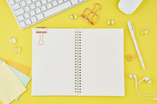 Blank notepad page in bullet journal on bright yellow office desktop. Top view of a modern bright table with notebook, stationery. Mock up, copy space, concept for diary