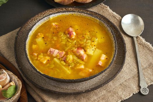 Winter hot soup with chopped green peas, pork, bacon, smoked on a dark brown wooden table. Delicious appetizing fat rich soup.