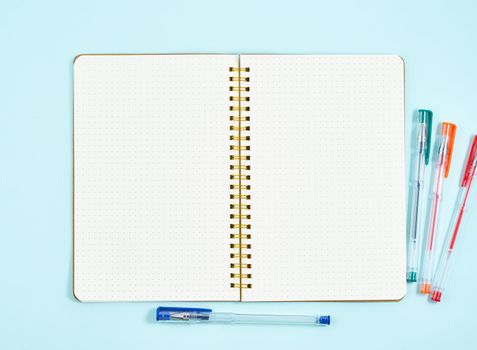 Blank notepad page in bullet journal on blue office desktop. Top view of modern bright table with notebook. Mock up, copy space.