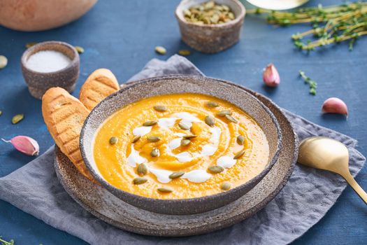 Pupmkin cream soup puree on dark bright blue wooden table, dietary vegetarian lunch, side view