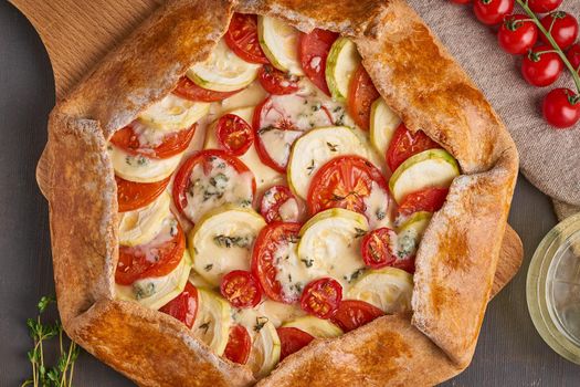 Homemade galette with vegetables, wholegrain pie with tomatoes, zucchini, cheese. Top view, close up. Dark brown table