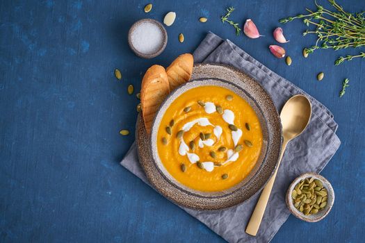 Pupmkin cream soup puree on dark blue wooden table, dietary vegetarian lunch, top view, copy space