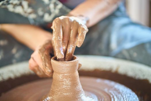 Woman making ceramic pottery on wheel, hands close-up, creation of ceramic ware. Handwork, craft, manual labor, dirty work