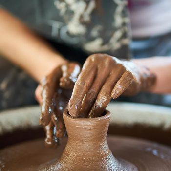 Woman making ceramic pottery on wheel, hands close-up, creation of ceramic ware. Handwork, craft, heavy dirty work
