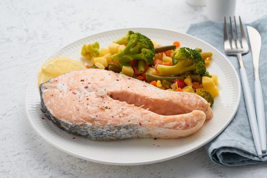 Steam salmon and vegetables, healthy diet. White plate on a concrete table, side view