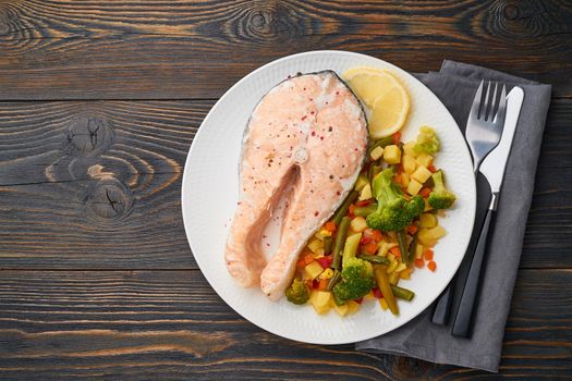 Steam salmon and vegetables, healthy diet. White plate on a rustic wooden table, top view, copy space