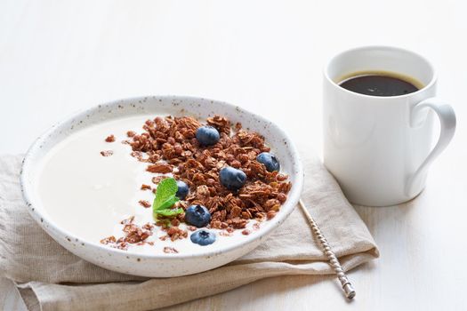 Yogurt with chocolate granola, bilberry. Breakfast with cupof coffee on white background, side view