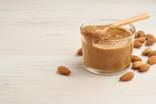 almond butter, raw food paste made from grinding almonds into a nut butter, crunchy and stir, white wooden table, copy space
