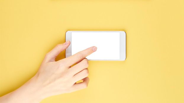 woman touching screen on mobile phone, blank screen to put your own web-page or message on it, yellow background top view