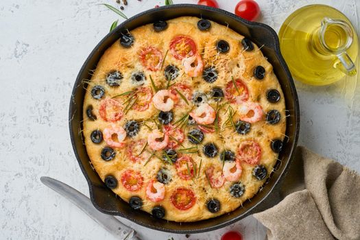 Focaccia, shrimp pizza in skillet, italian flat bread with tomatoes, olives and a rosemary. Top view, copy space, white concrete background