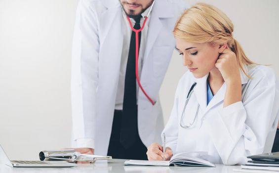 Doctor at hospital office writes notes on patients report while having conversation with another doctor that standing beside her.