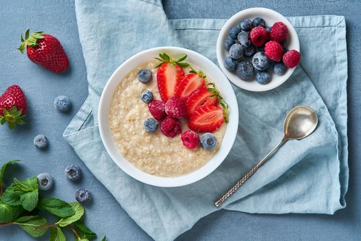 Oatmeal with blueberry, strawberry, raspberry on blue dark background. Top view. Healthy diet breakfast