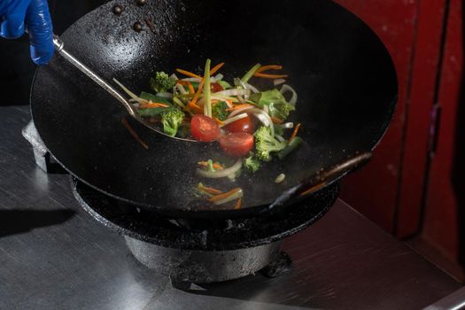 Frying vegetables in a wok pan onions, broccoli, tomatoes cherry, carrot, asparagus.