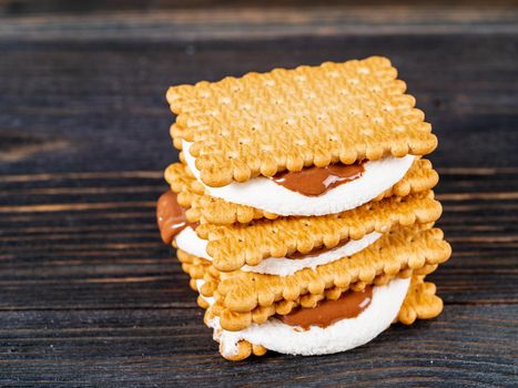 Smores, marshmallow sandwiches - traditional American sweet chocolate cookies on dark wooden table, side view