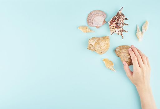 vacation and holiday mockup, travel concept, female hands holding big seashell on aquamarine background top view copy space