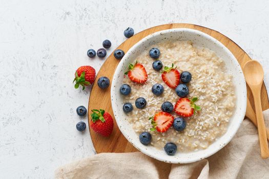 Oatmeal rustic porridge with blueberry, bilberry, blackberry, strawberry, dash diet, wooden white background top view copy space