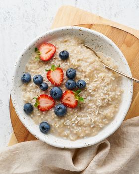 Oatmeal rustic porridge with blueberry, bilberry, blackberry, strawberry, dash diet, wooden white background top view closeup