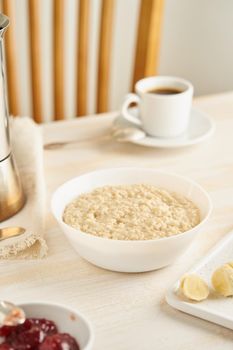 Oatmeal, large bowl of tasty healthy porridge for breakfast, morning meal. Vertical, side view, white wooden rustic table. Vegan diet