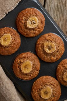 Banana muffin in tray, top view, vertical. Cupcakes on old linen napkin, rustic wooden table, breakfast with cake