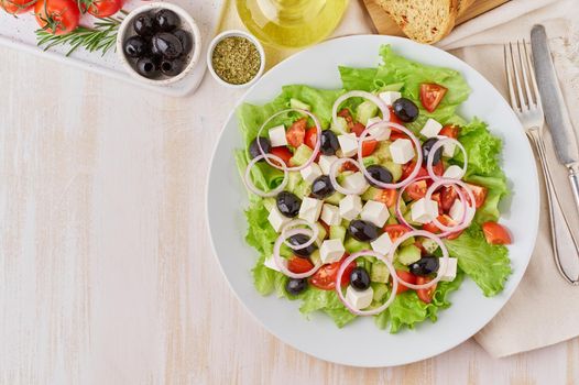 Greek salad on white plate on old rustic white wooden table, fresh salad with tomatoes, cucumbers, feta, onion. Top view, copy space