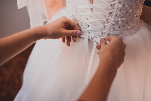 The back of the bride in a wedding dress. Mom's and woman's hands help fasten the clasps at the back.