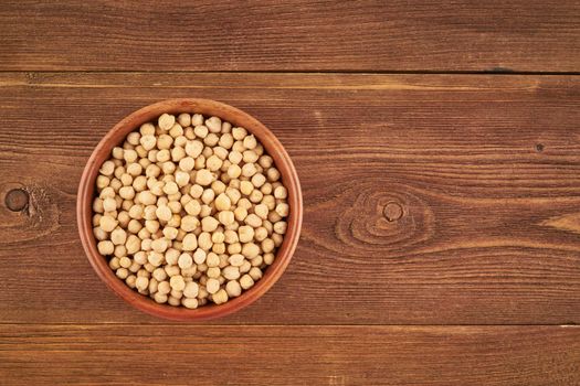 Dried chickpea in wooden bowl on brown background, top view, copy space, close up