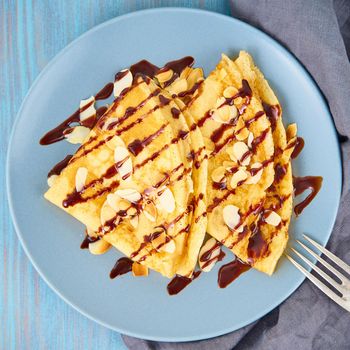 Two pancakes with chocolate syrup, almond flakes on plate, honey flows from spoon, top view, macro