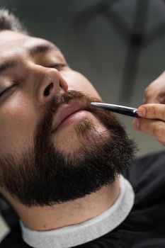 Haircut beard with scissors for a gentleman in a trendy barbershop. Professional hairdresser.