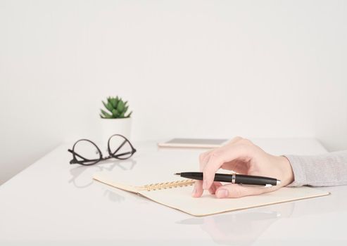 female young hand holding pen and writing on notebook page on white and gray background side view copy space