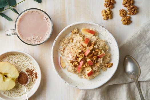 Oatmeal with apple, nuts, honey and cup of chocolate on white wooden light background. Top view. Healthy diet breakfast