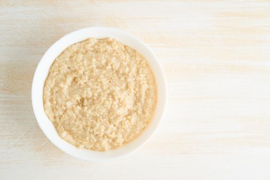 Oatmeal, large bowl of tasty healthy porridge for breakfast, morning meal. Top view, copy space, close up, white wooden rustic table. Vegan diet