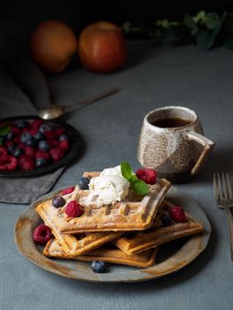 Belgian waffles with raspberries, chocolate syrup. Breakfast with tea on dark background, side view, vertical