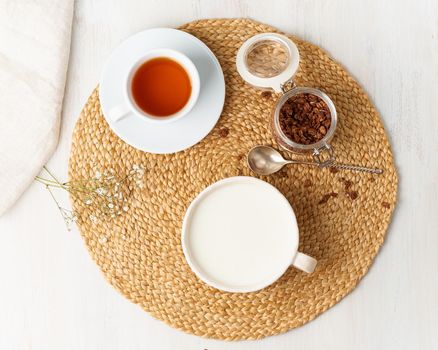 Yogurt with chocolate granola in cup, breakfast with tea on beige background, top view