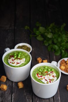Broccoli cream soup on dark wooden background, vertical, copy space. Vegetable green puree in two large white cup. Diet vegan soup of broccoli, zucchini, green peas
