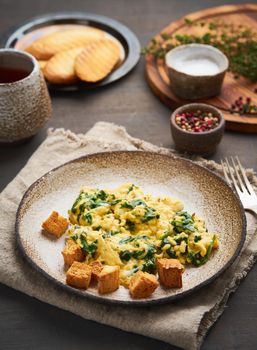 Scrambled eggs with spinach, cup of tea on dark brown background. Vertical. Breakfast with Pan-fried omelette, side view, close up