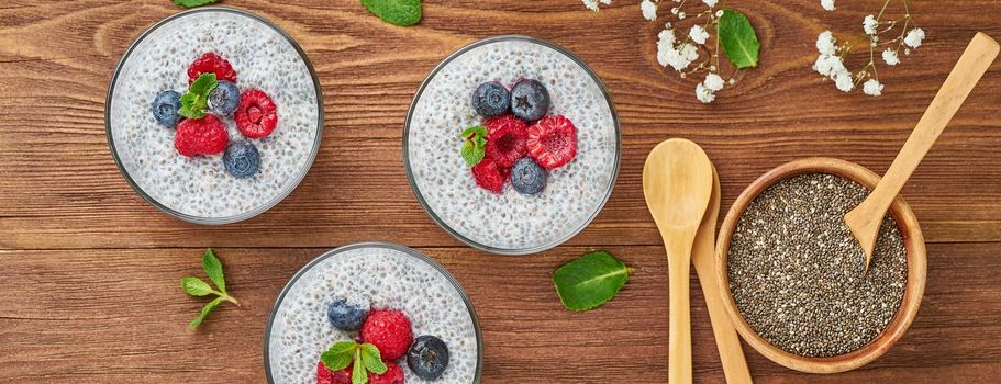 Long banner with Chia pudding with fresh berries raspberries, blueberries. Top view, brown wooden background