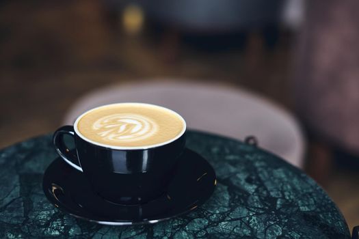A Cup of cappuccino with foam on a marble table near window in a cozy little cafe. Drink with vegetable milk, oatmeal, coconut. Side view, copy space